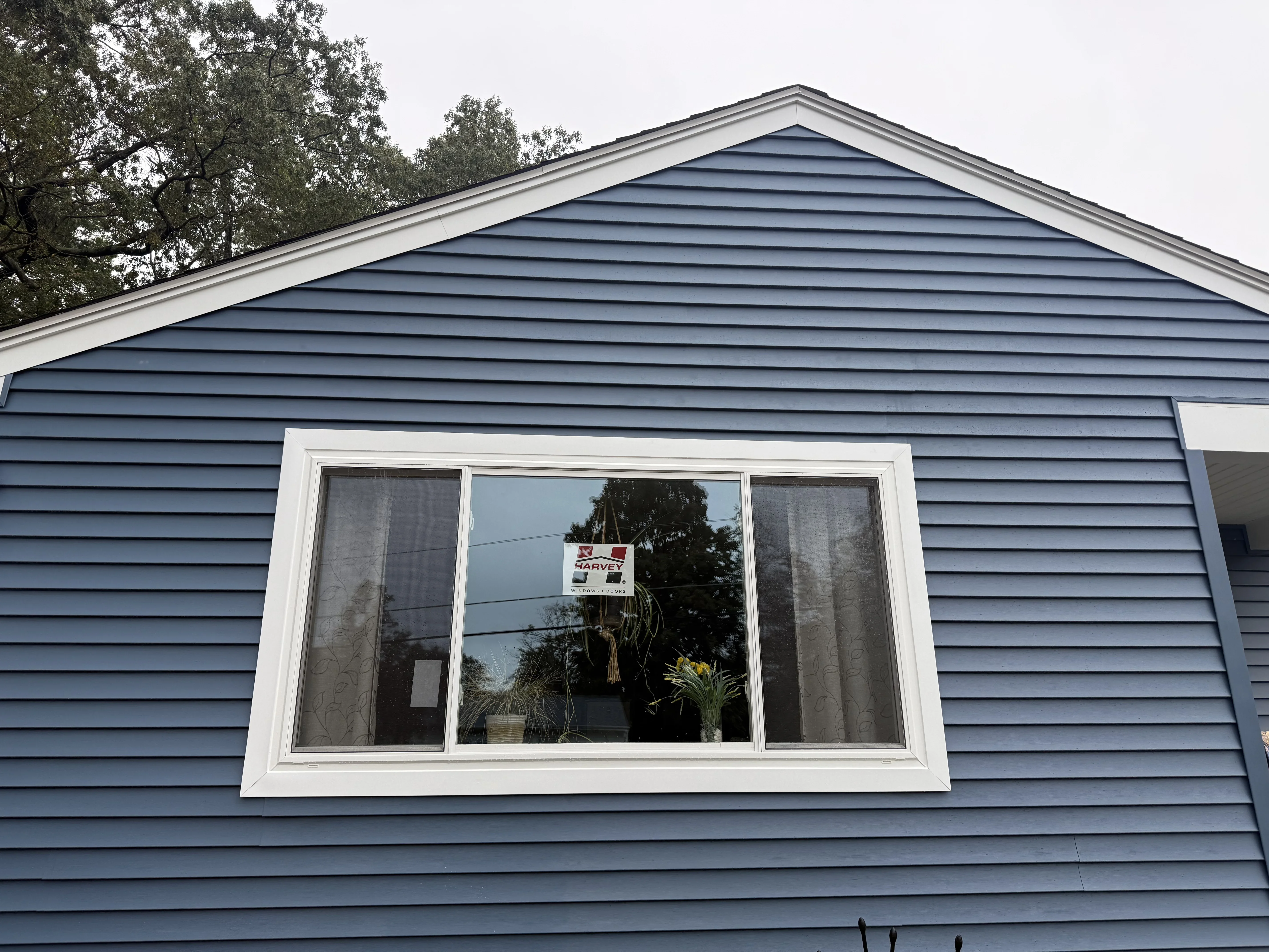 Gable roof with metal panels, blue horizontal siding, and three-panel picture window with white trim